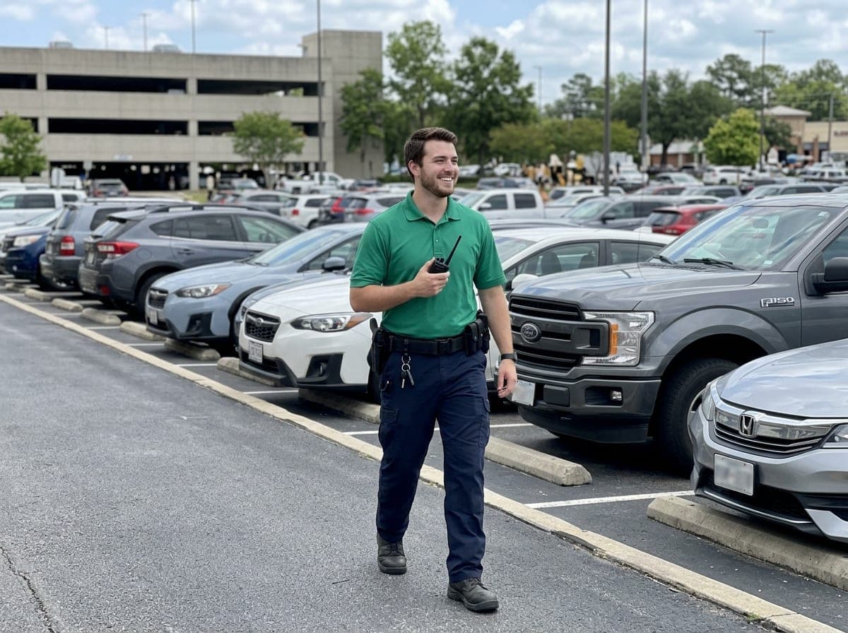 A uniformed patrol guard walking a parking lot at dusk on a scheduled route.