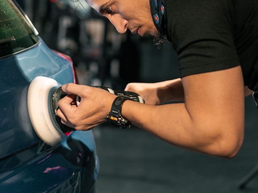 A detailer machine polishing a vehicle panel in the bay