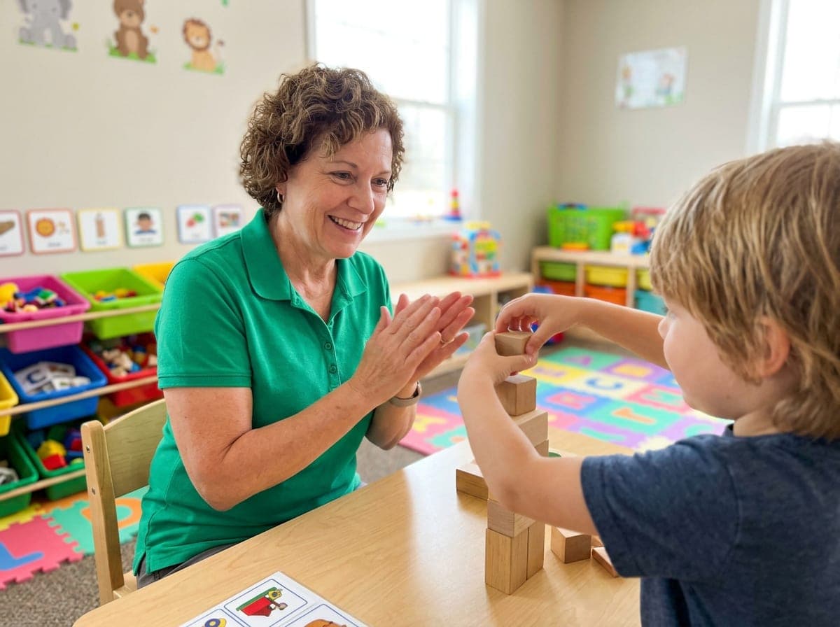 A behavior therapist and a child working at a small table with educational materials, while a supervisor observes nearby in a clinic.